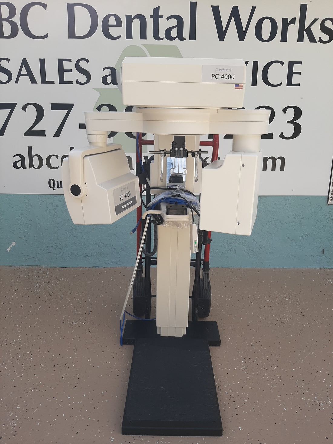 Panoramic PC-4000 panoramic X-ray unit, full front view of the column, rotating arm and patient footplate, standing outdoors on pavement.