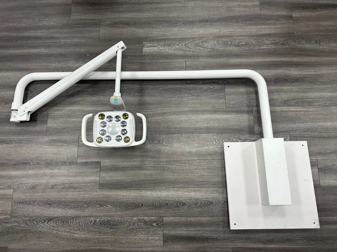 A-dec 575L LED dental light disassembled on a floor: light head with rigid arm, second arm section and white wall mount bracket plate.