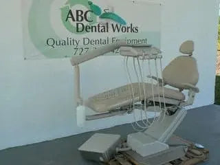 A-dec 1021 Decade chair in beige upholstery with radius delivery unit, handpiece tubing and foot control, staged by the ABC Dental Works banner