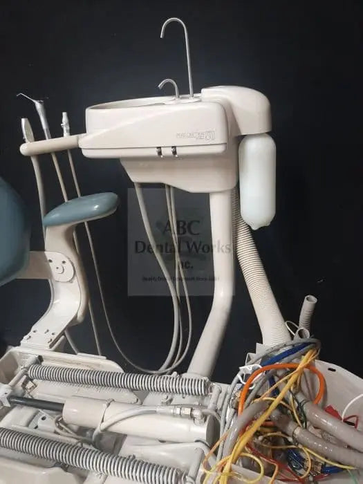 A-dec 8000 chairside cuspidor and support center with cup filler and assistant's holders, loose wiring at the base; teal dental chair behind is staging