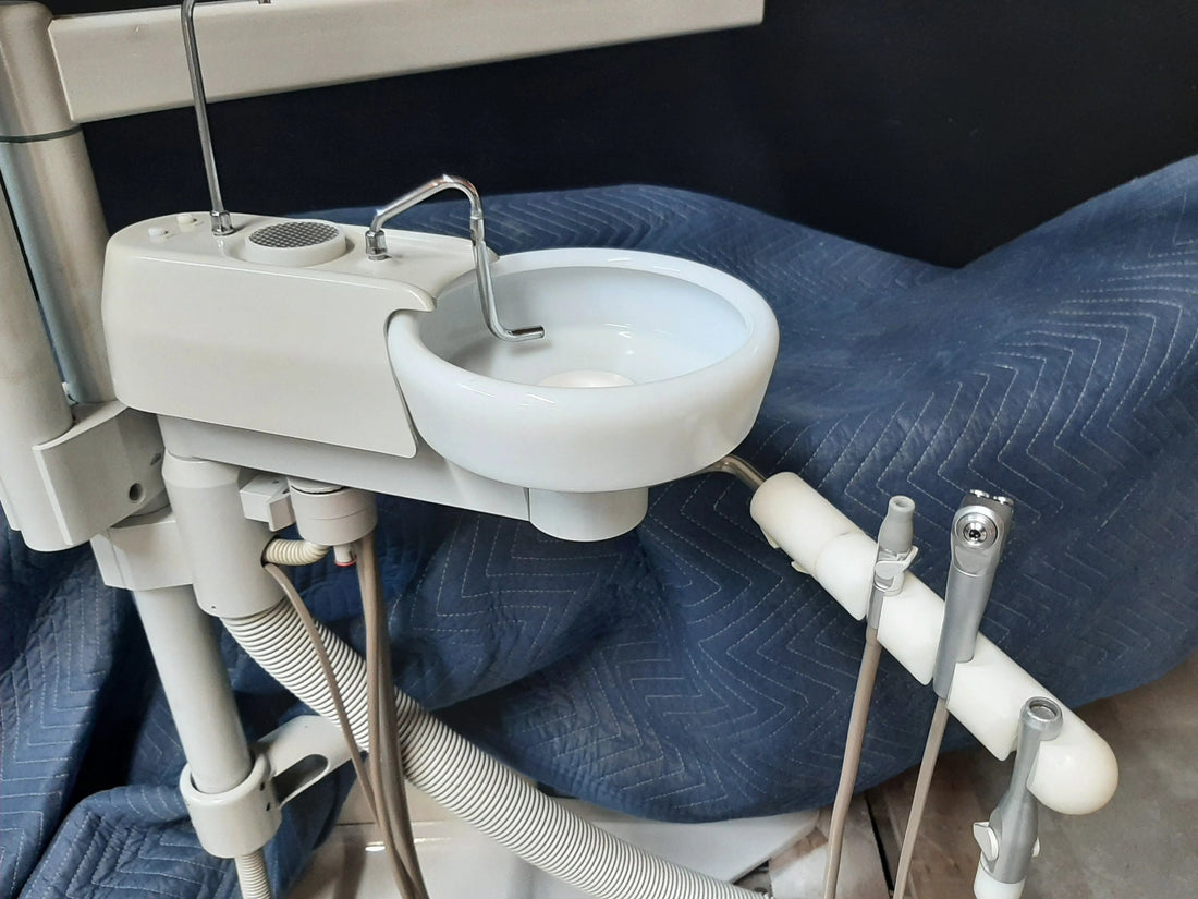 Forest post-mounted cuspidor on a blue moving blanket, porcelain bowl and cup filler faucet, vacuum hose below and assistant's HVE and syringe tips at right