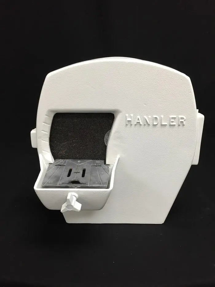 Handler dental model trimmer, white cast housing with raised HANDLER lettering, dark abrasive wheel exposed above the cast metal work table and water valve