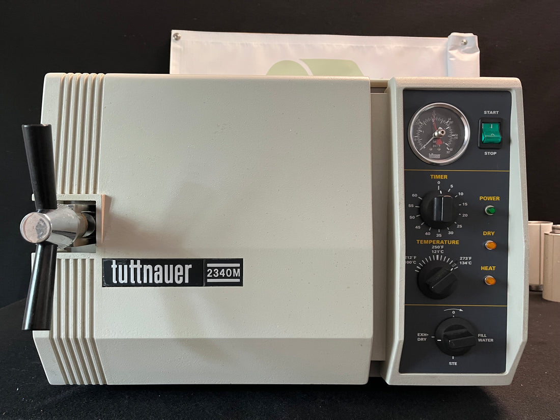 Tuttnauer 2340M autoclave, front view with the door closed, black handle, pressure gauge and control panel, on a black backdrop.