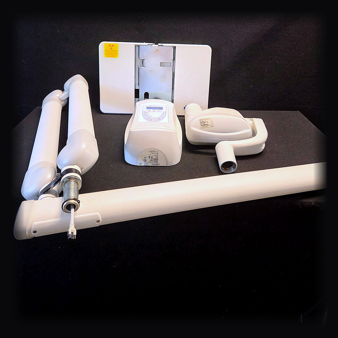 Refurbished Midmark Progeny Preva intraoral X-ray system laid out on a black backdrop: wall mount backplate, LCD exposure control panel, tube head with cone, horizontal extension arm and articulating scissor arm