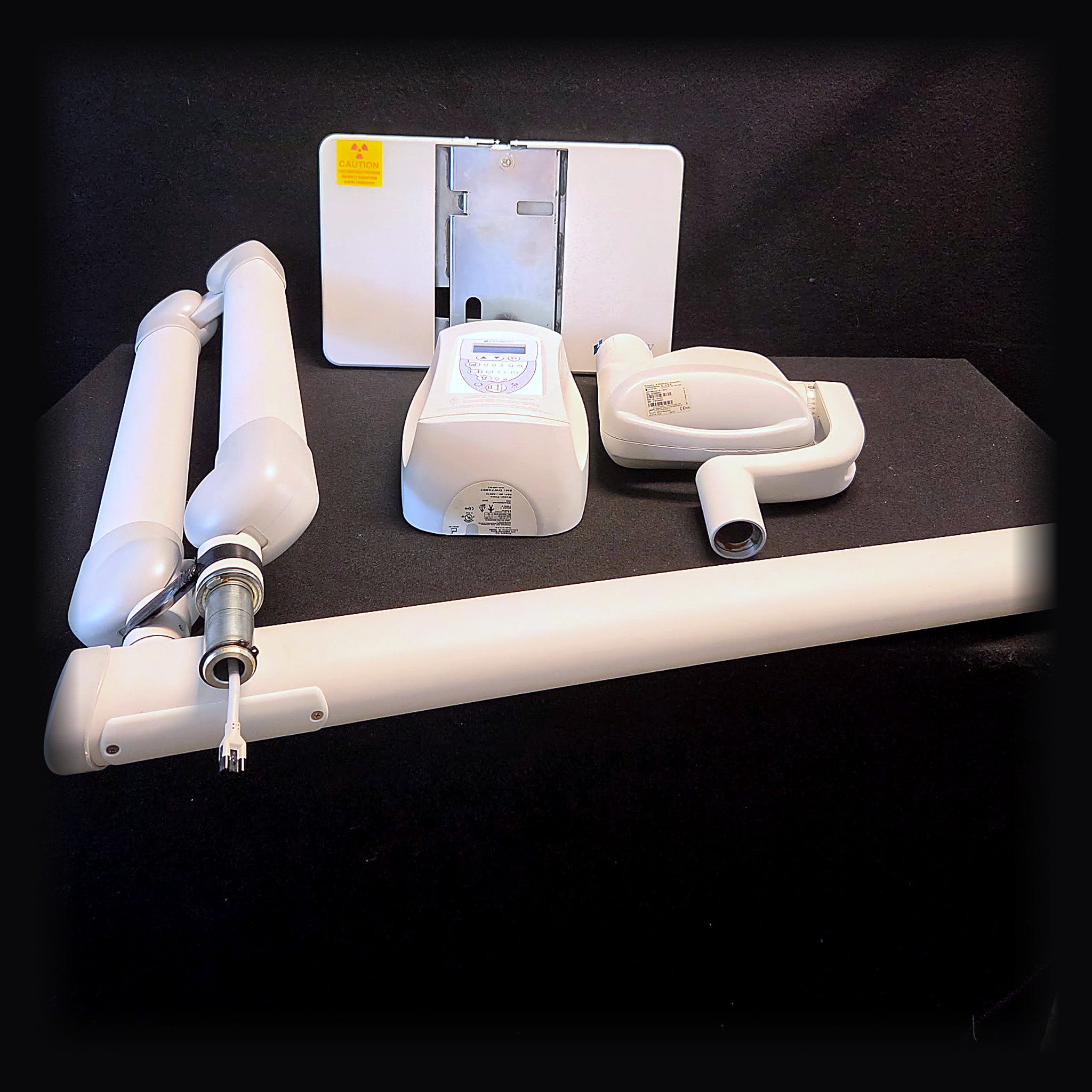 Refurbished Midmark Progeny Preva intraoral X-ray system laid out on a black backdrop: wall mount backplate, LCD exposure control panel, tube head with cone, horizontal extension arm and articulating scissor arm