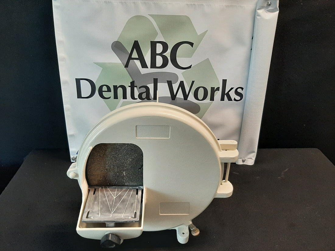 Ray Foster 12 inch dental model trimmer, front view of the wheel hood, work table and cast base on a bench with shop banner behind.