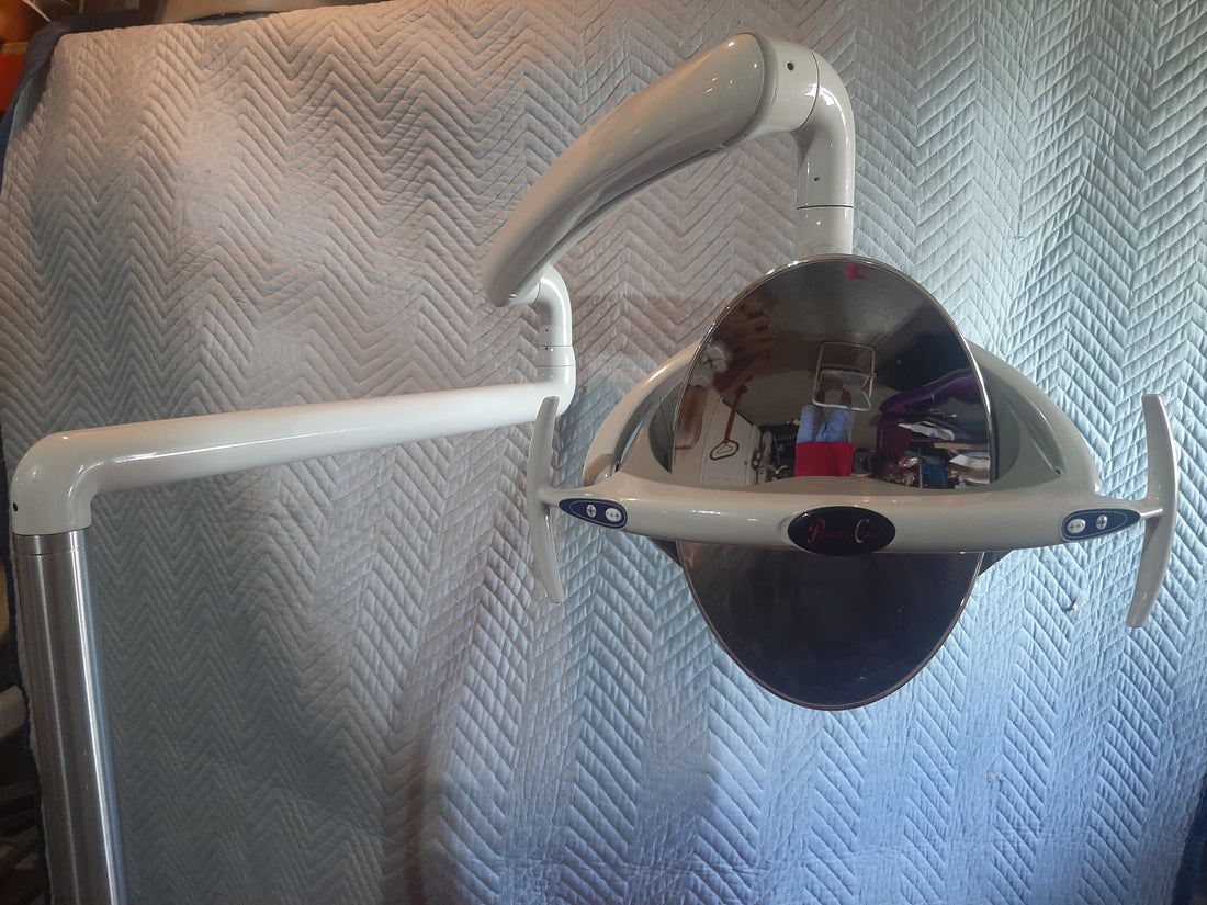 Pelton & Crane Helios 1800 LED operatory light head on its post-mounted arm, reflector dome and handle wings, shot against a moving blanket.