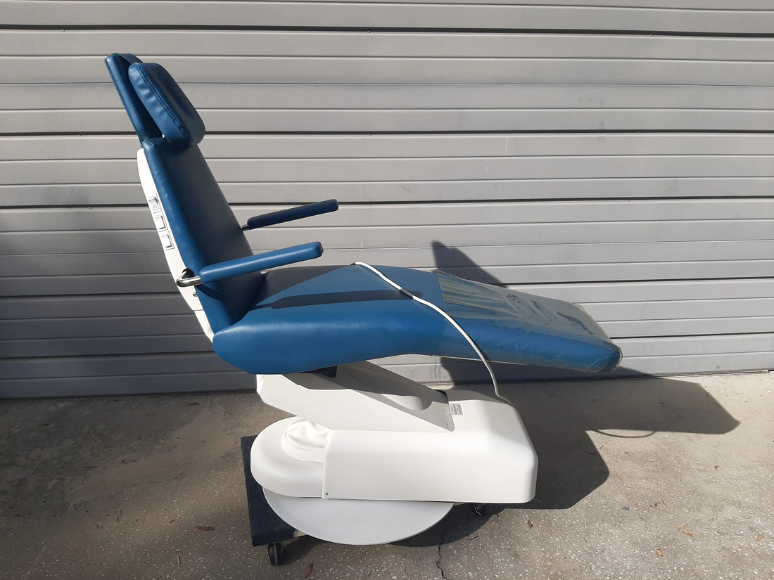 Royal PD2 pediatric dental chair, left side view outdoors against a metal door, blue upholstery strapped for transport; no delivery unit or light shown.