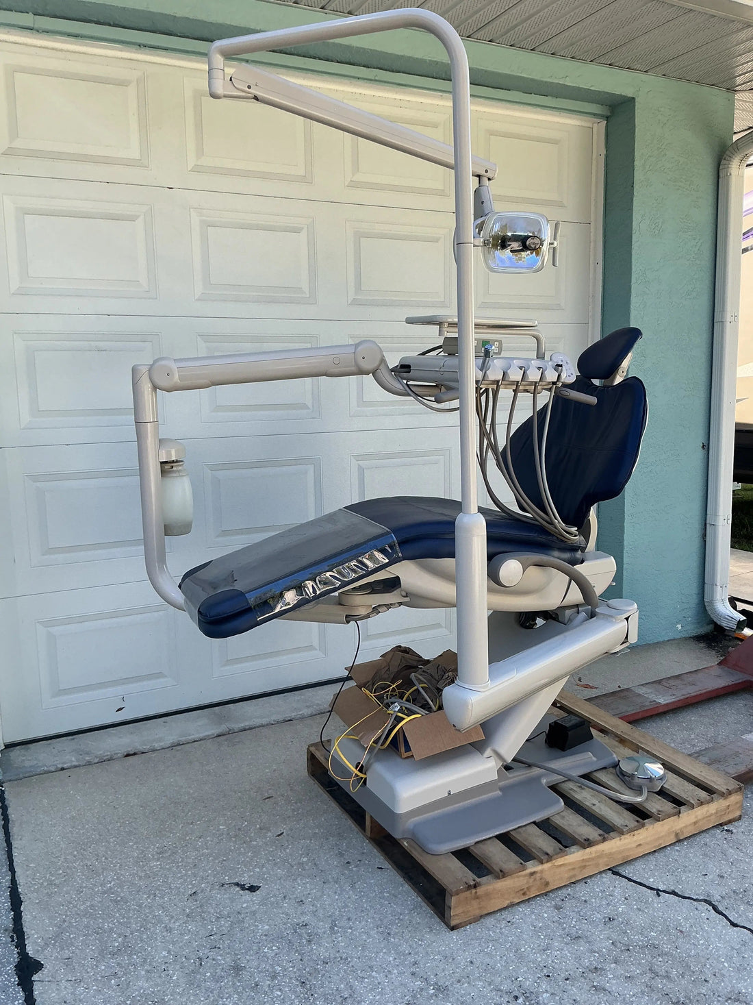 A-dec 511 dental chair with navy upholstery on a shipping pallet outdoors, with continental delivery unit, assistant arm and overhead light.