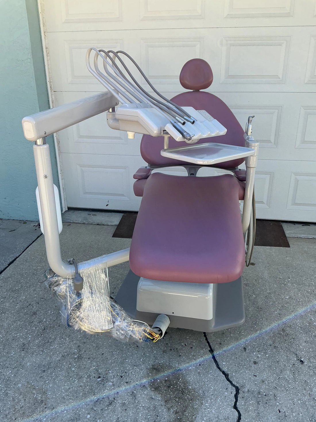 A-dec Cascade 1040 dental chair in mauve upholstery outdoors on concrete, continental delivery unit and assistant arm, tubing taped for shipping.