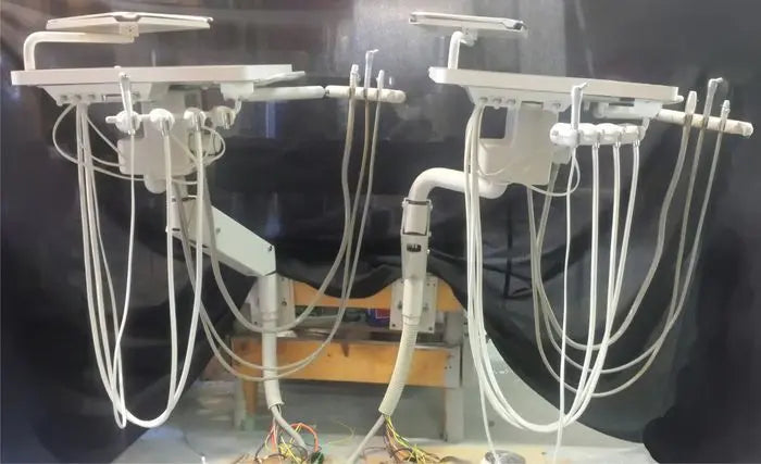 Two A-dec rear delivery units set up side by side on a bench, each with a tray, flex arm and four instrument tubings, wiring exposed at the base