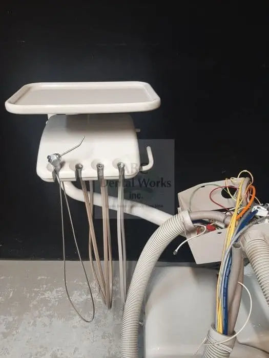 A-dec Performer 8000 Radius delivery unit uninstalled on a shop floor, tray raised, four handpiece tubings hanging beside a coiled umbilical hose