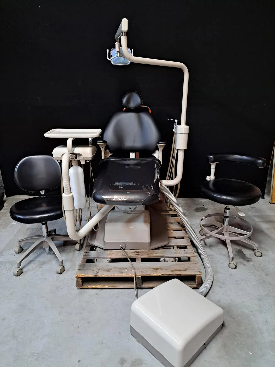 A-dec Performer 8000 package on a pallet: black upholstered chair, euro delivery, A-dec 6300 light and side tray; two stools and a cabinet nearby are staging.