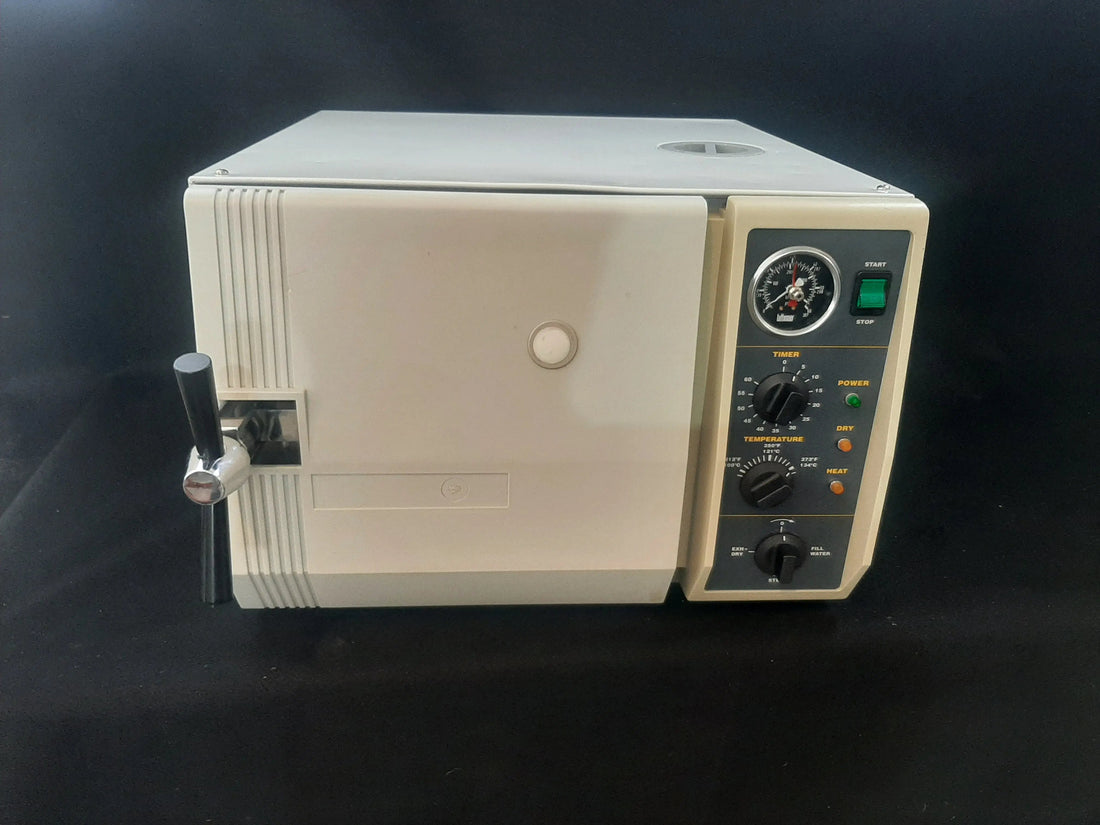 Tuttnauer 2540M autoclave, front left three-quarter view, chamber door closed with the black locking handle bar extended at left.